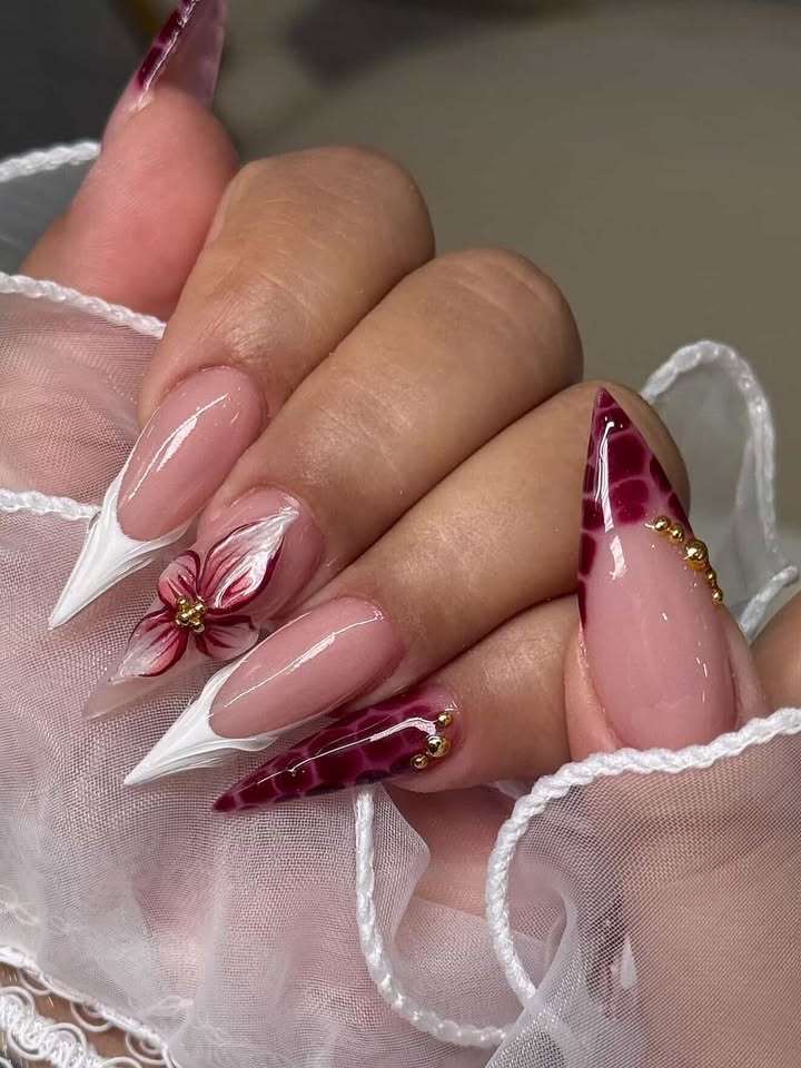 Stiletto nails with deep red marble tips and 3D floral accent