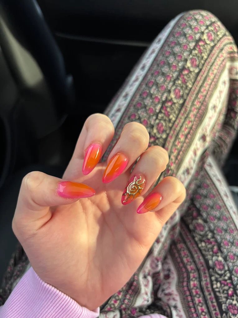 Bright pink to orange ombre nails with a gold swirl charm accent